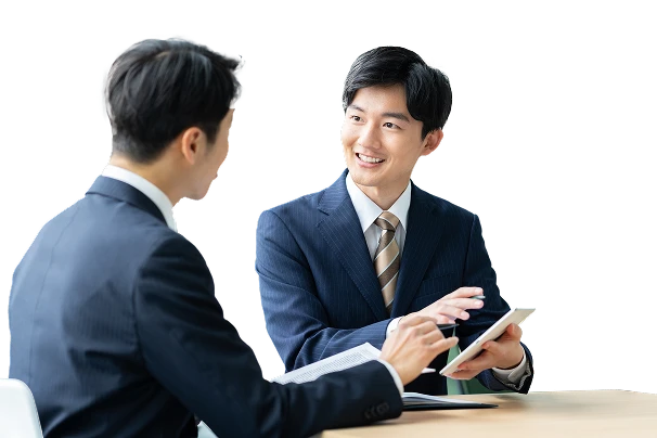 赤い背景の前で、タブレットを指して笑顔で説明する男性と、熱心に聞くもう一人の男性の商談風景。